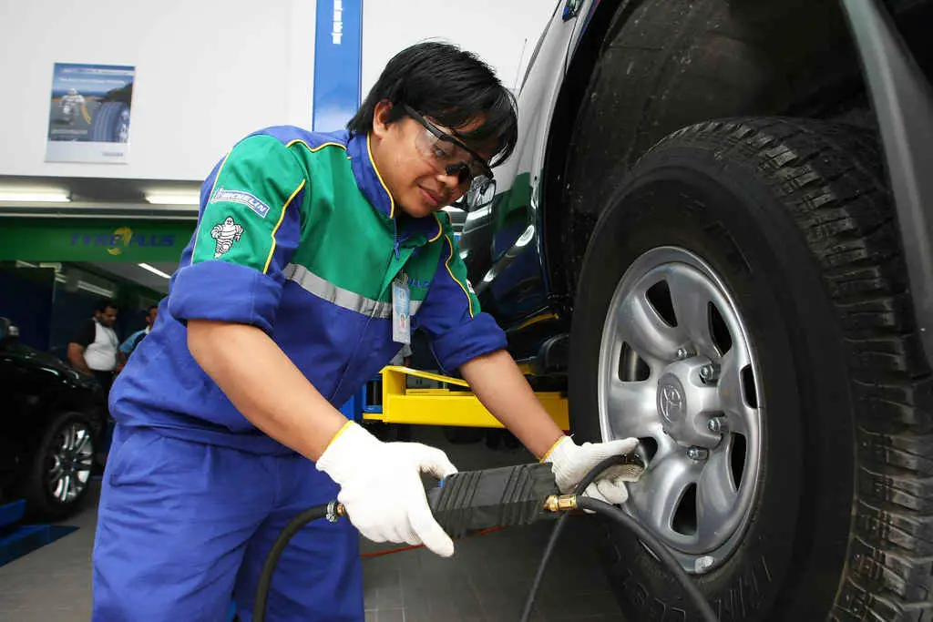 UK Car Maintenance. a female engineer on green top and blue trouser with glove using tire inflator to fill air into a car tire
