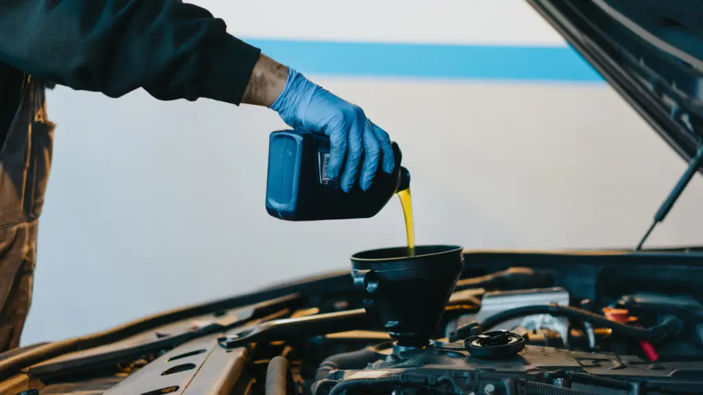 a man on glove pouring oil into a car engine.