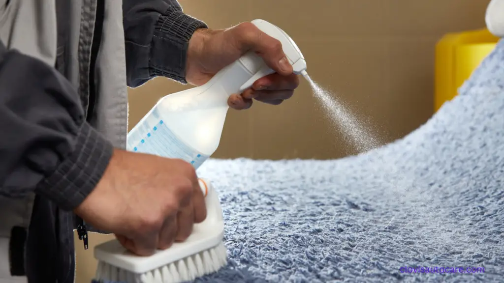 A man using stain remover with brush to clean car fabric